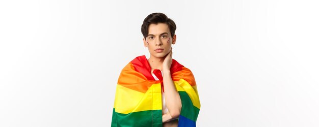 Coup de taille d'un bel homme gay avec des paillettes sur le visage s'envelopper avec le drapeau lgbt arc-en-ciel et toucher