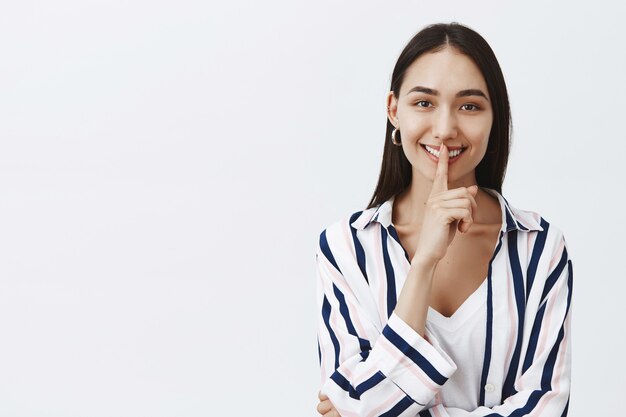 Coup de taille d'une belle femme belle en chemisier rayé sur un t-shirt, souriant largement tout en disant chut, faisant un geste chut avec l'index sur la bouche, disant un secret à un ami