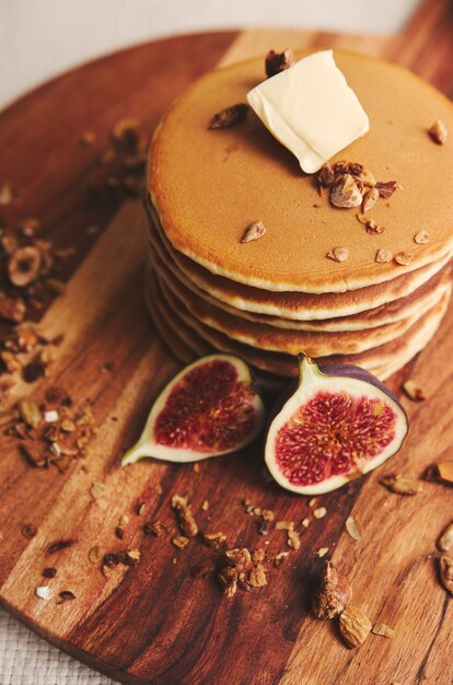 Coup vertical de crêpes au sirop, beurre, figues et noix grillées sur une plaque en bois