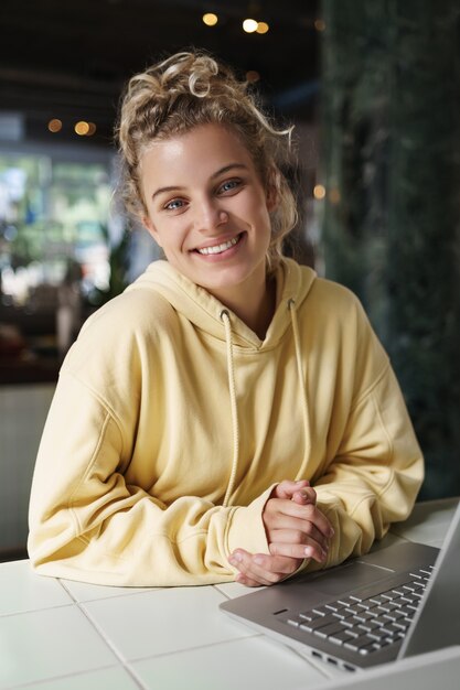 Coup vertical d'une femme souriante heureuse assis dans un café avec un ordinateur portable.