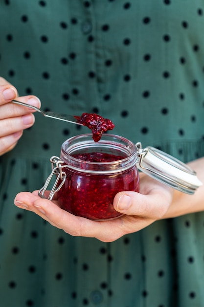 Photo gratuite coup vertical de mains féminines tenant une confiture de framboises crues vegan maison dans un bocal en verre