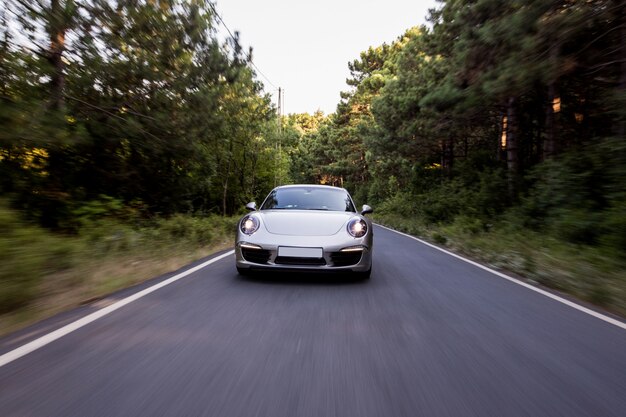 Coupe couleur argent avec feux avant allumés sur la route.