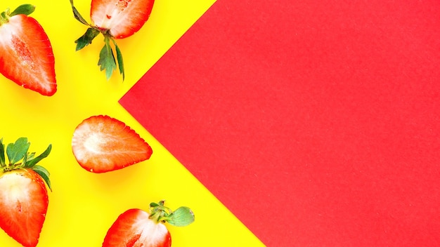 Photo gratuite coupé dans une moitié de fraises et un papier rouge sur fond jaune