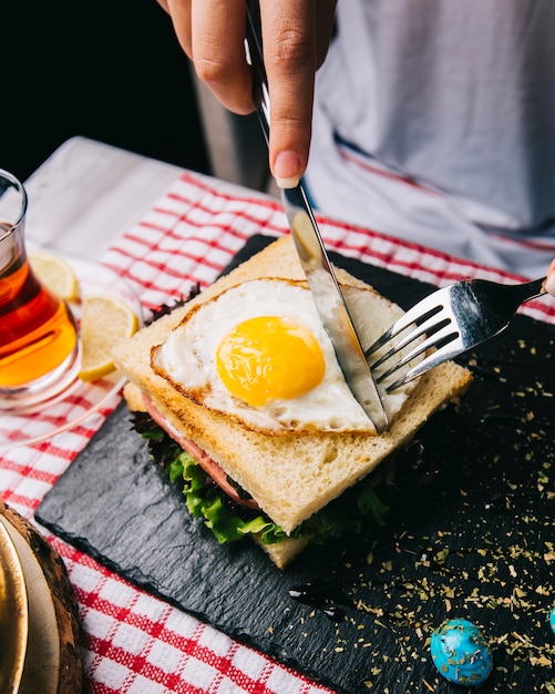 Coupe sandwich avec oeuf au plat avec un couteau et une fourchette.