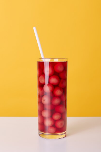 Coupe en verre de cocktail rouge avec tube à boire et cerises isolé sur fond jaune, boisson d'été non alcoolisée fraîche sur la table.