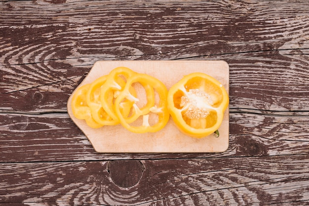 Couper en deux et tranches de poivron jaune sur une planche à découper sur le fond de texture en bois