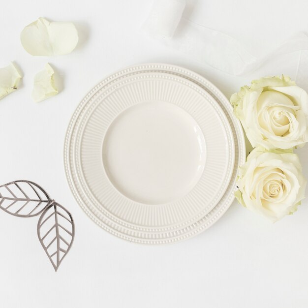 Couper les feuilles; roses et assiette en céramique; ruban sur fond blanc