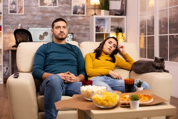 Couple acclamant leur équipe préférée en regardant la télévision et en mangeant de la restauration rapide