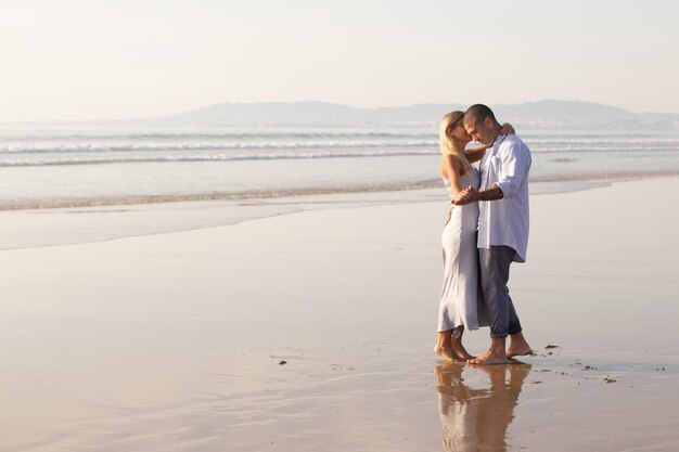 Un couple actif d'hommes et de femmes passe du temps à la plage. Mari et femme en vêtements décontractés s'embrassant et dansant le jour de l'été. Vacances, bonheur, concept de relation