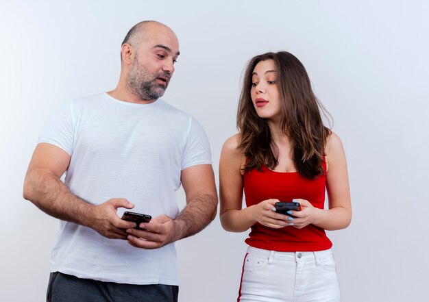 Couple d'adultes impressionné à la fois tenant des téléphones mobiles et se regardant les téléphones de l'autre