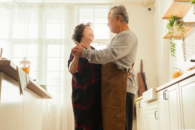 Photo gratuite couple d'adultes seniors asiatiques cuisinant des aliments sains ensemble à la maison tout en dansant dans la cuisine le week-end du matin