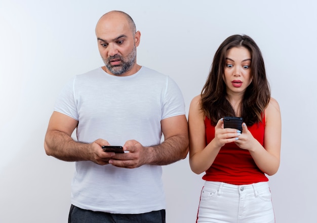 Couple d'adultes surpris à la fois tenant et regardant leurs téléphones mobiles