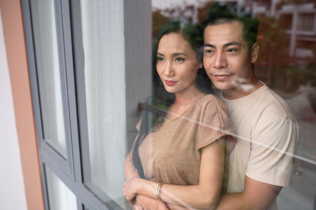 Photo gratuite couple affectueux embrassant et regardant par la fenêtre à la maison