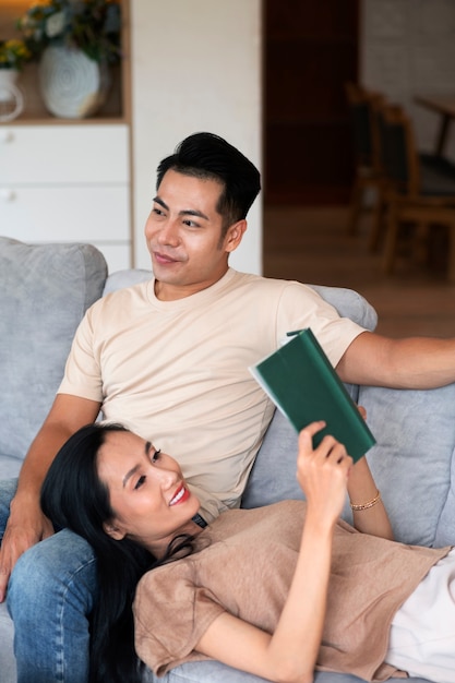 Couple affectueux à la maison sur le canapé en lisant un livre et en prenant un verre