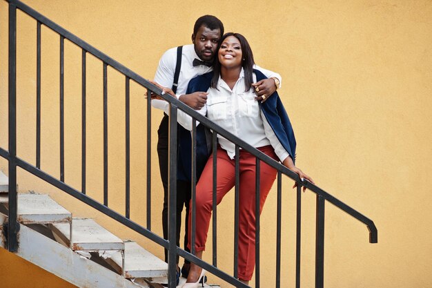 Couple afro-américain élégant en tenue de soirée Couple romantique amoureux datant contre un mur jaune dans les escaliers