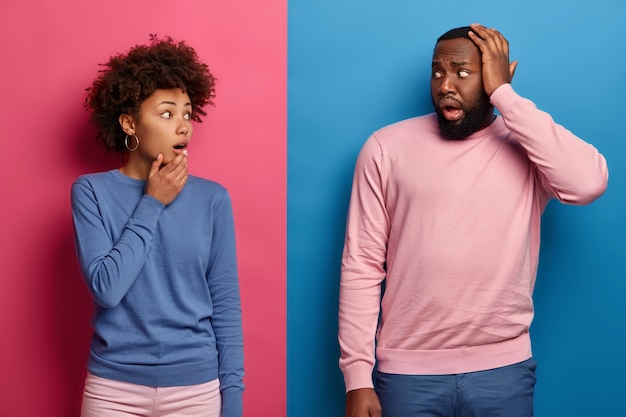 Un couple afro stupéfait se regarde avec embarras, a des problèmes, réfléchit ensemble à la résolution du problème, a les yeux bouchés, la peau foncée