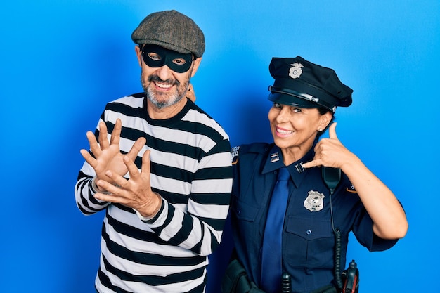 Photo gratuite couple d'âge moyen d'une femme hispanique et d'un homme portant un uniforme de voleur et de police souriant faisant un geste téléphonique avec la main et les doigts comme parler au téléphone. notions communicantes.