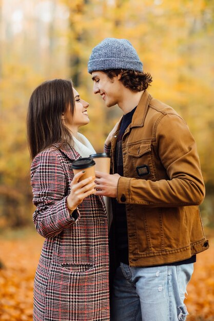 Un couple amoureux d'écharpes est assis dans un parc, tenant des tasses de thé ou de café