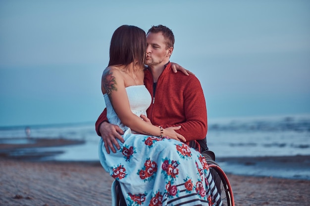 Un couple d'amoureux, une femme assise sur les genoux de son mari, s'embrassant sur une plage sur fond d'aube lumineuse.