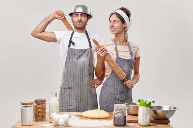 Photo gratuite couple amoureux occupé à cuisiner en famille, avoir confiance en lui à la cuisine, préparer la pâte pour préparer la tarte, avoir tous les ingrédients nécessaires, tenir le rouleau à pâtisserie, préparer la fête. nourriture, cuisine, concept de recette