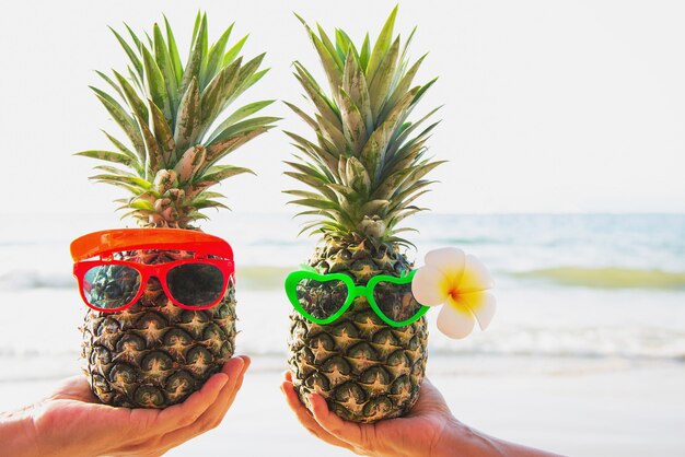 Couple d'ananas frais mettant des lunettes dans les mains d'un touriste avec la vague de la mer - amour heureux et amusement avec le concept de vacances en bonne santé