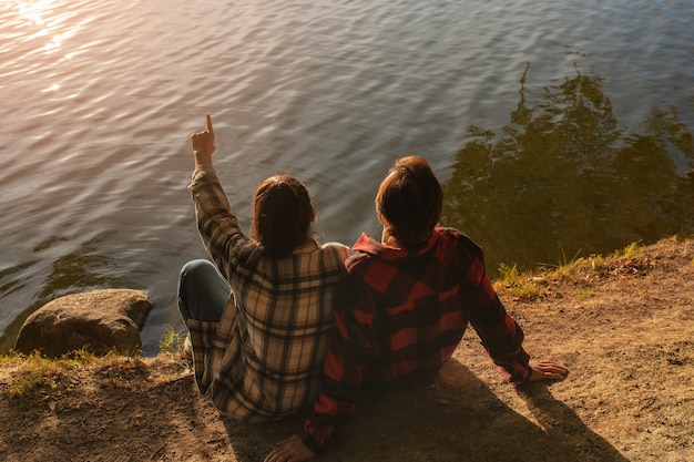 Photo gratuite couple à angle élevé assis au bord du lac