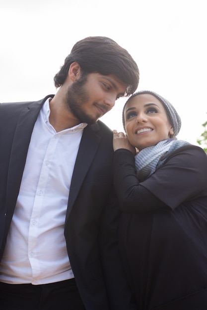 Couple arabe amoureux marchant ensemble. Femme avec tête couverte et maquillage lumineux s'appuyant sur l'épaule de son petit ami, levant les yeux. Amour, concept d'affection