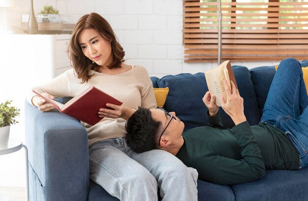 un couple asiatique passe le week-end ensemble sur un canapé à la maison à se détendre et à lire un livre
