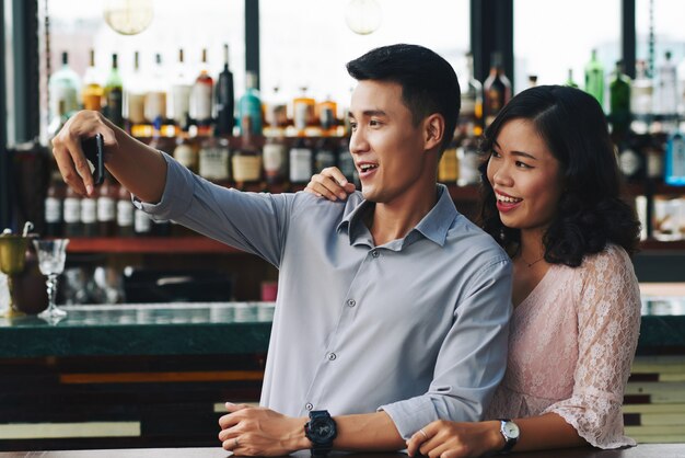 Couple asiatique prenant selfie sur smartphone au bar