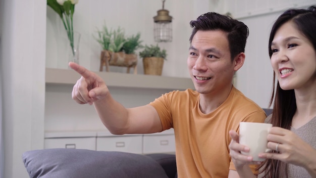 Couple asiatique en regardant la télévision et en buvant une tasse de café dans le salon à la maison, profitez d&#39;un couple