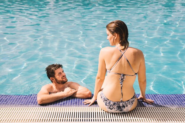 Couple assis à bord de la piscine en train de parler