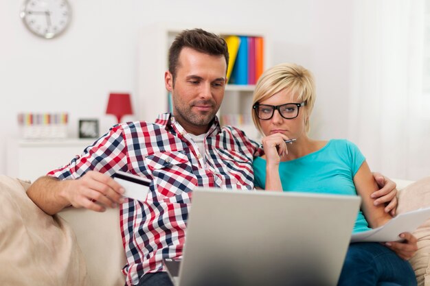 Couple assis sur un canapé à la maison et payer la facture en ligne