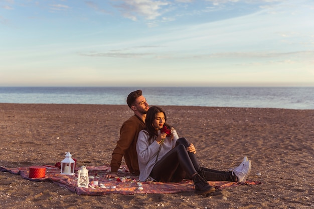 Couple assis sur une couverture au bord de la mer de sable