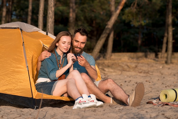 Photo gratuite couple assis installant une caméra près d'une tente