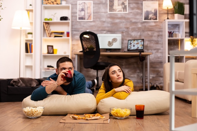 Couple assis par terre et regardant la télévision dans leur salon.