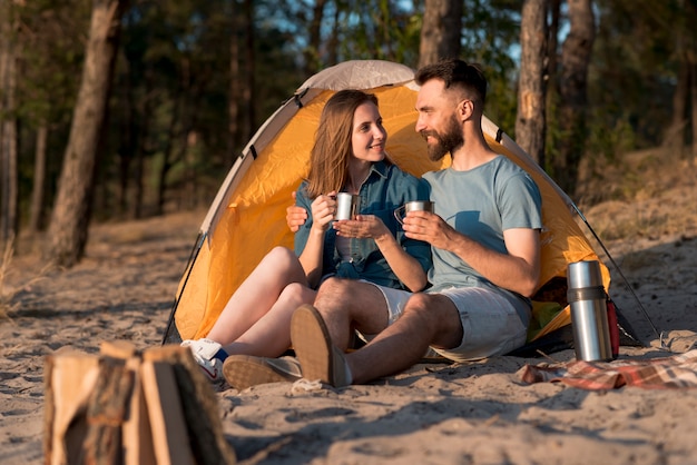 Photo gratuite couple assis près de la tente et buvant