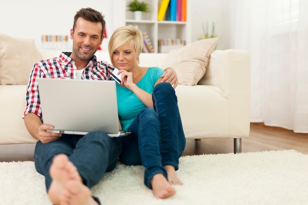 Couple Assis Sur Un Tapis à La Maison Et Faire Des Achats En Ligne