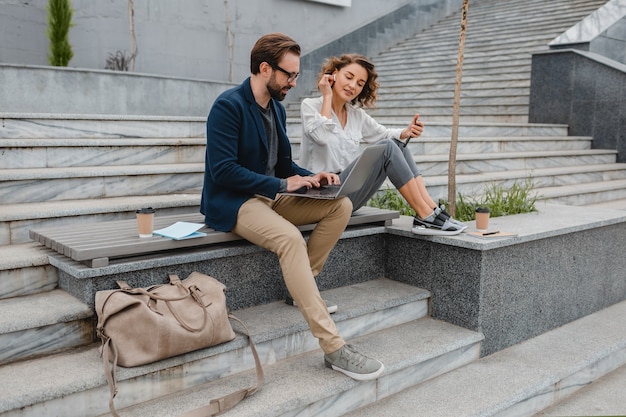 Couple attrayant d'homme et de femme assis dans les escaliers du centre-ville urbain, travaillant ensemble sur un ordinateur portable