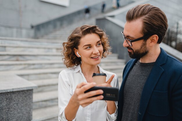 Couple attrayant d'homme et de femme parlant dans le centre-ville urbain, tenant le téléphone et regardant