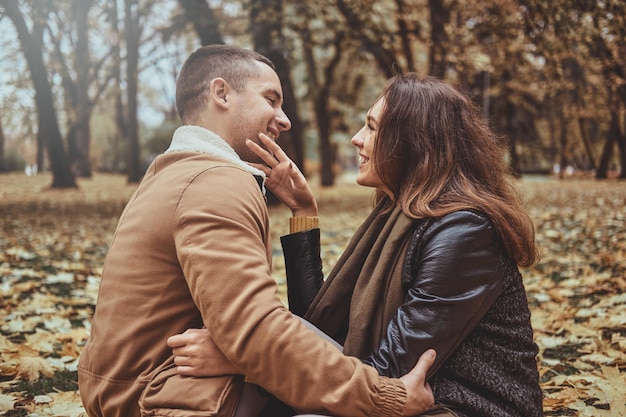 Photo gratuite un couple attrayant s'amuse tout en étant assis dans un parc d'automne plein de feuilles dorées.