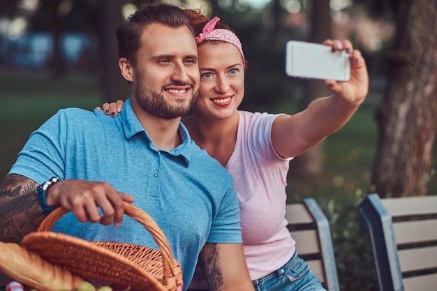 Un couple attrayant et souriant prenant un selfie lors d'un pique-nique dans un parc, lors d'une rencontre à l'extérieur.