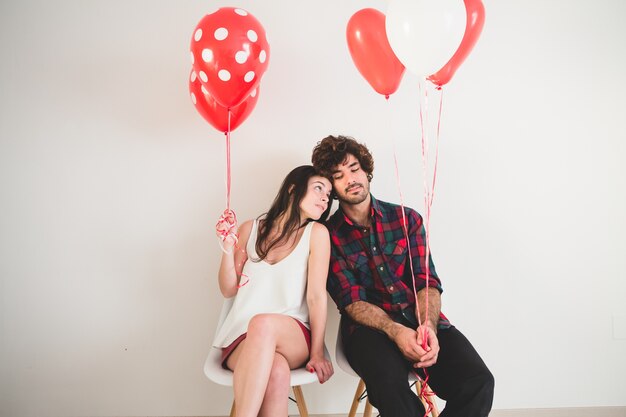Photo gratuite couple avec des ballons dans les mains assis sur des chaises blanches
