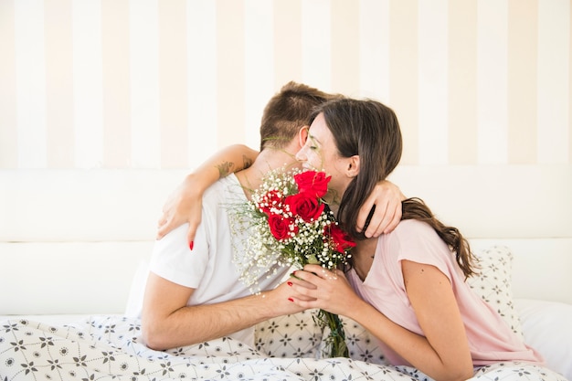 Couple avec bouquet embrassant au lit