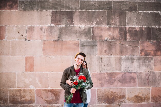 Couple avec bouquet près de mur de briques