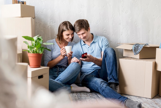 Couple avec café et smartphone lors de l'emballage pour déménager