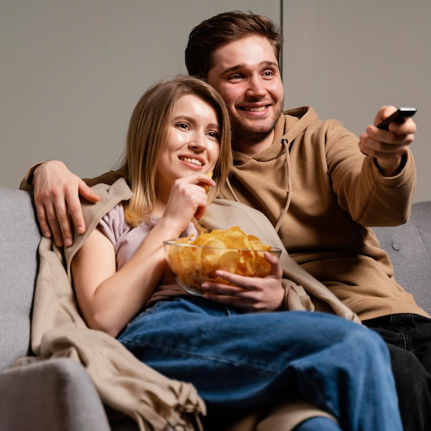 Couple sur canapé à regarder la télévision et manger des chips
