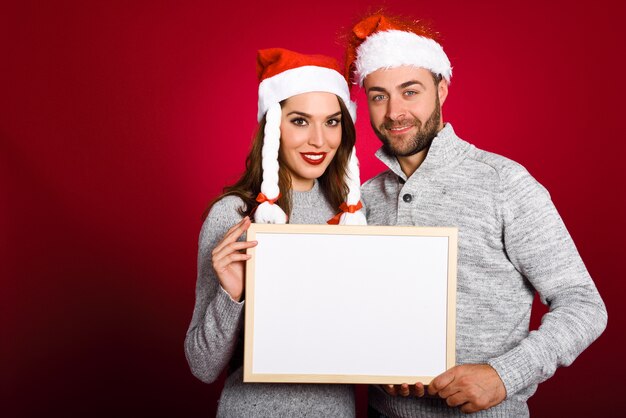 Couple avec un chapeau de père noël tenant tableau blanc