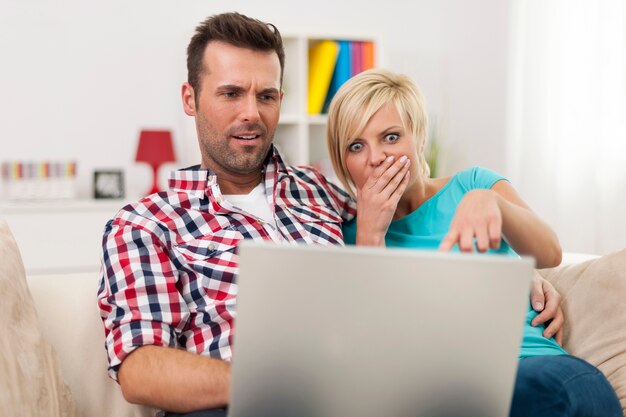 Couple choqué assis sur un canapé et regardant un ordinateur portable