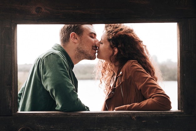 Photo gratuite couple sur le côté s'embrasser à côté d'une fenêtre en bois