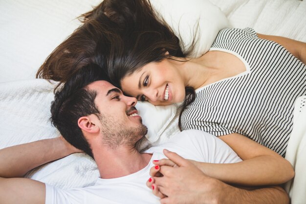 Couple couché sur le lit tenant la main et regardant dans les yeux les uns des autres